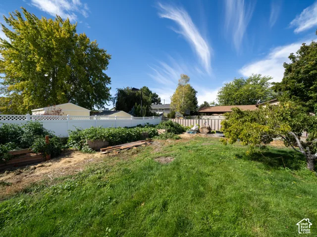 Expansive backyard featuring a lush lawn, mature trees, white lattice-top fencing, and raised garden beds