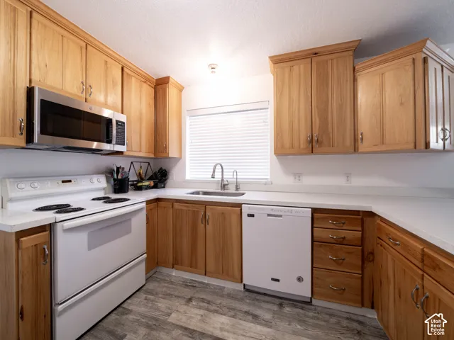 Kitchen featuring wood cabinetry, white countertops, a stainless steel microwave, a white electric range, and wood-finish flooring