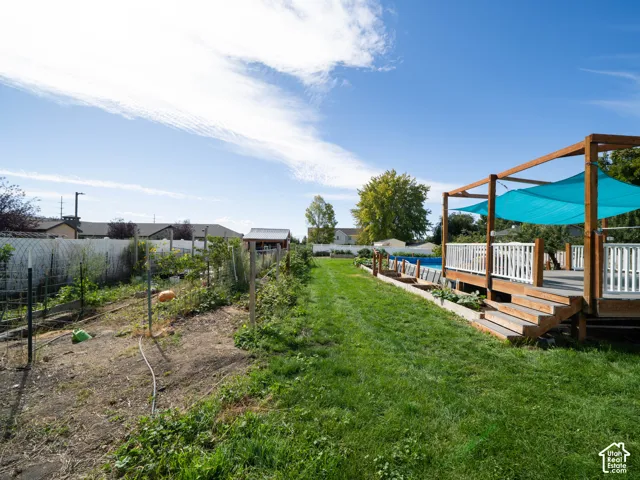 Expansive backyard featuring a manicured lawn, dedicated garden beds, and a wood deck with a pergola and white railing