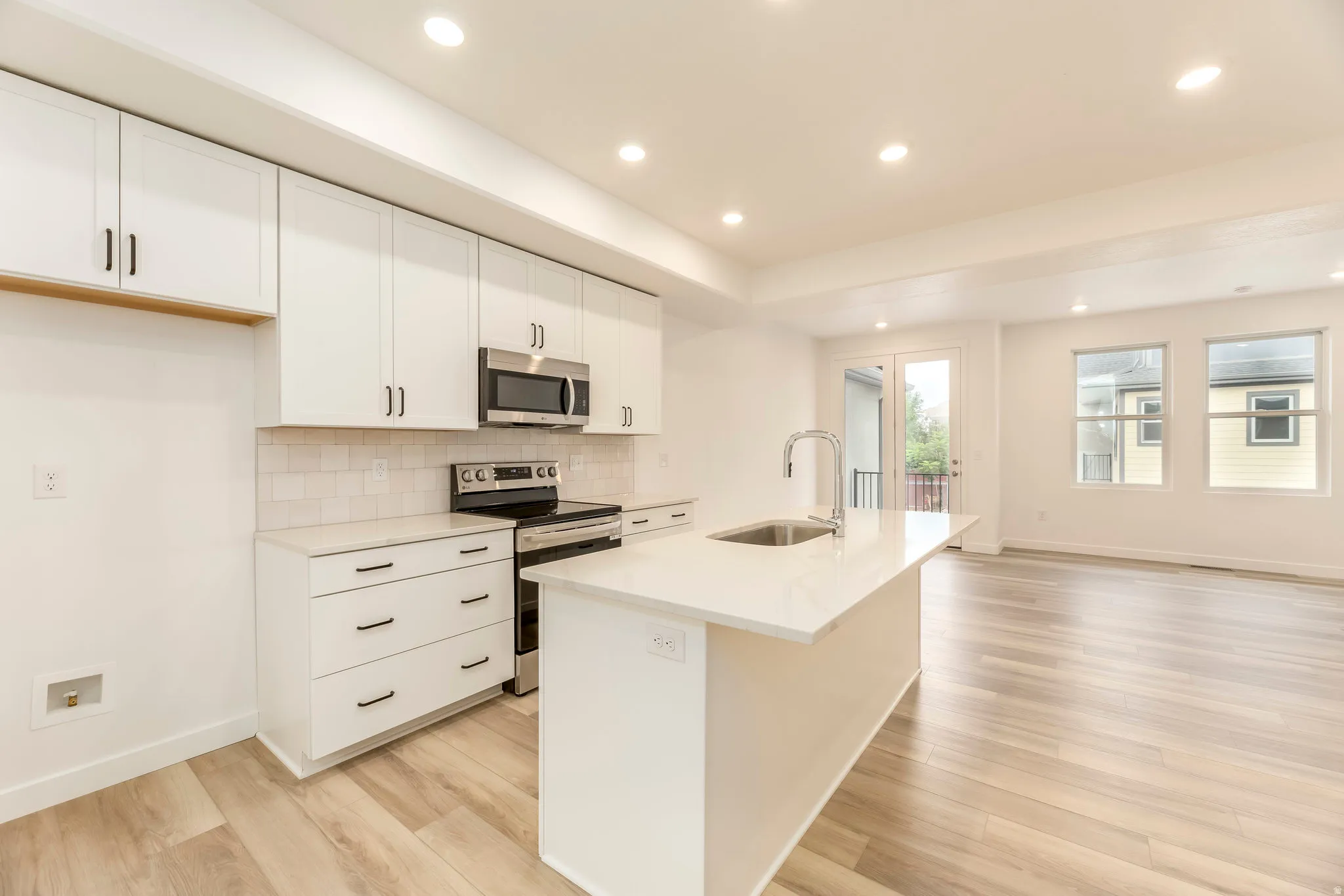 Kitchen with white cabinetry, stainless steel appliances, a center island with sink, and wood-finish flooring