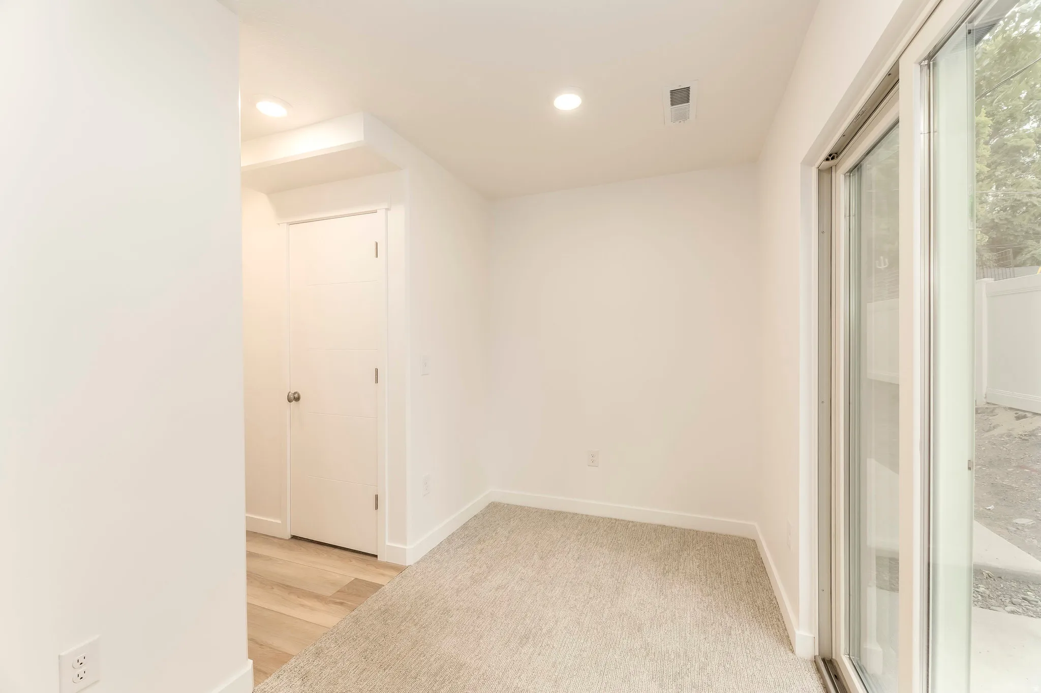 Recessed lighting, wood-finish flooring, light carpet, white walls, and a glass sliding door