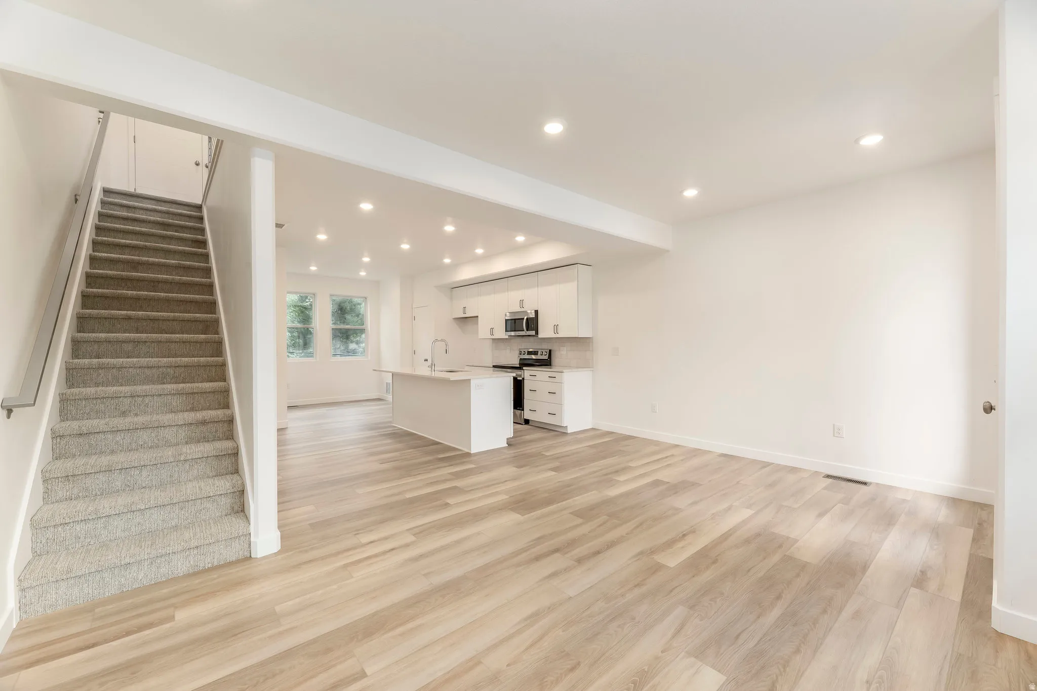 Recessed lighting, wood-finish flooring, white cabinetry, stainless steel appliances, and a central island with sink