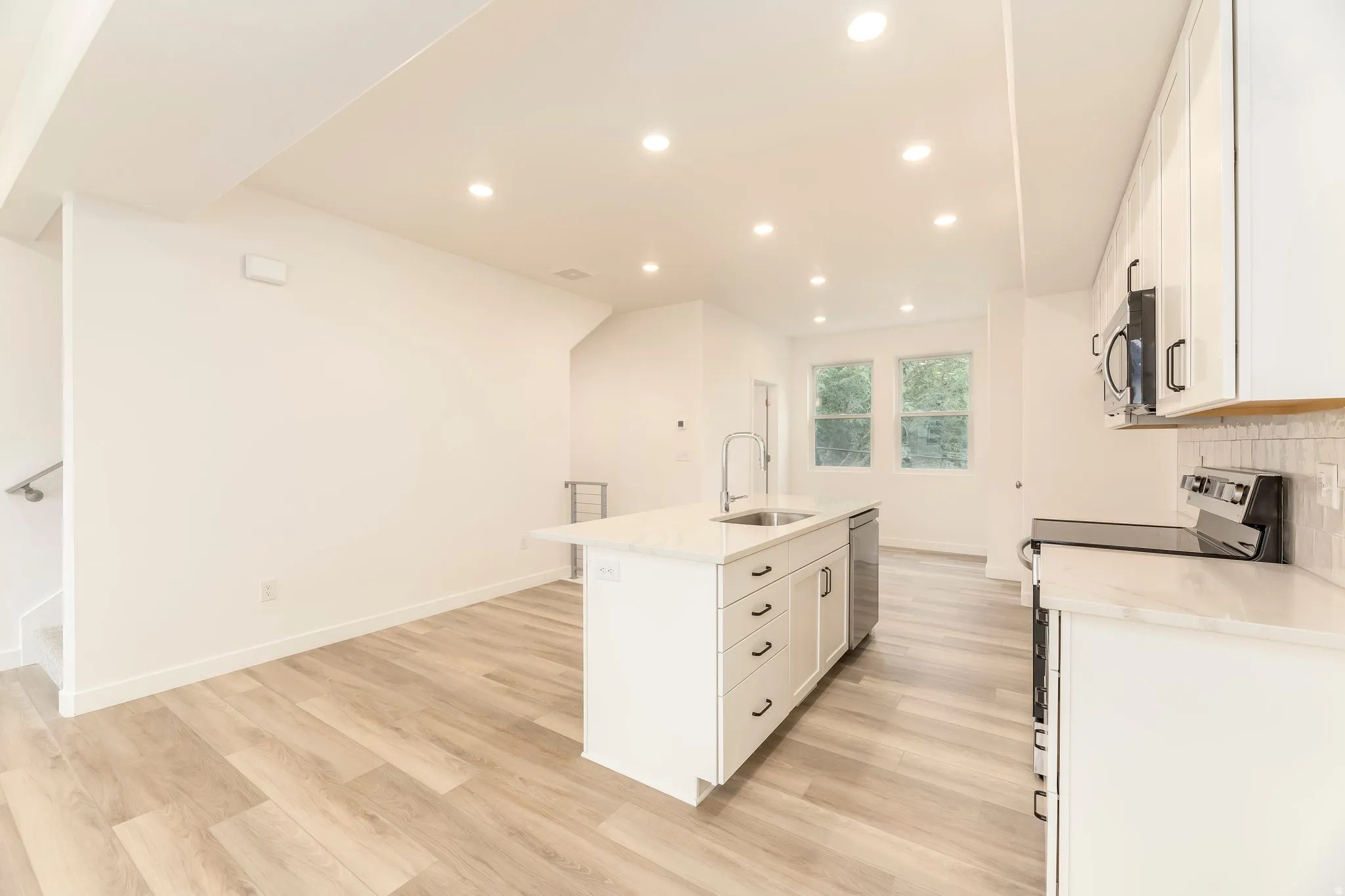 Open-concept living space with wood-finish flooring, recessed lighting, white cabinetry, a kitchen island with a sink, and stainless steel appliances
