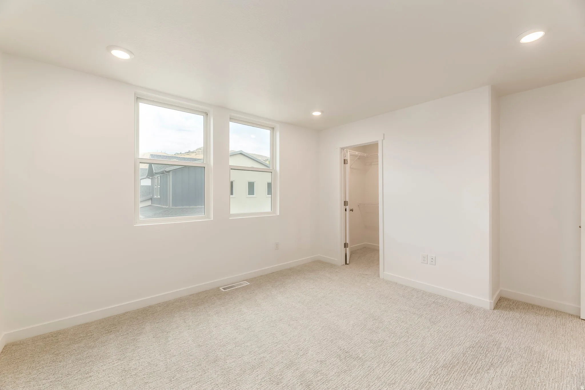 Recessed lighting illuminates this carpeted room featuring two windows and a closet with a bi-fold door