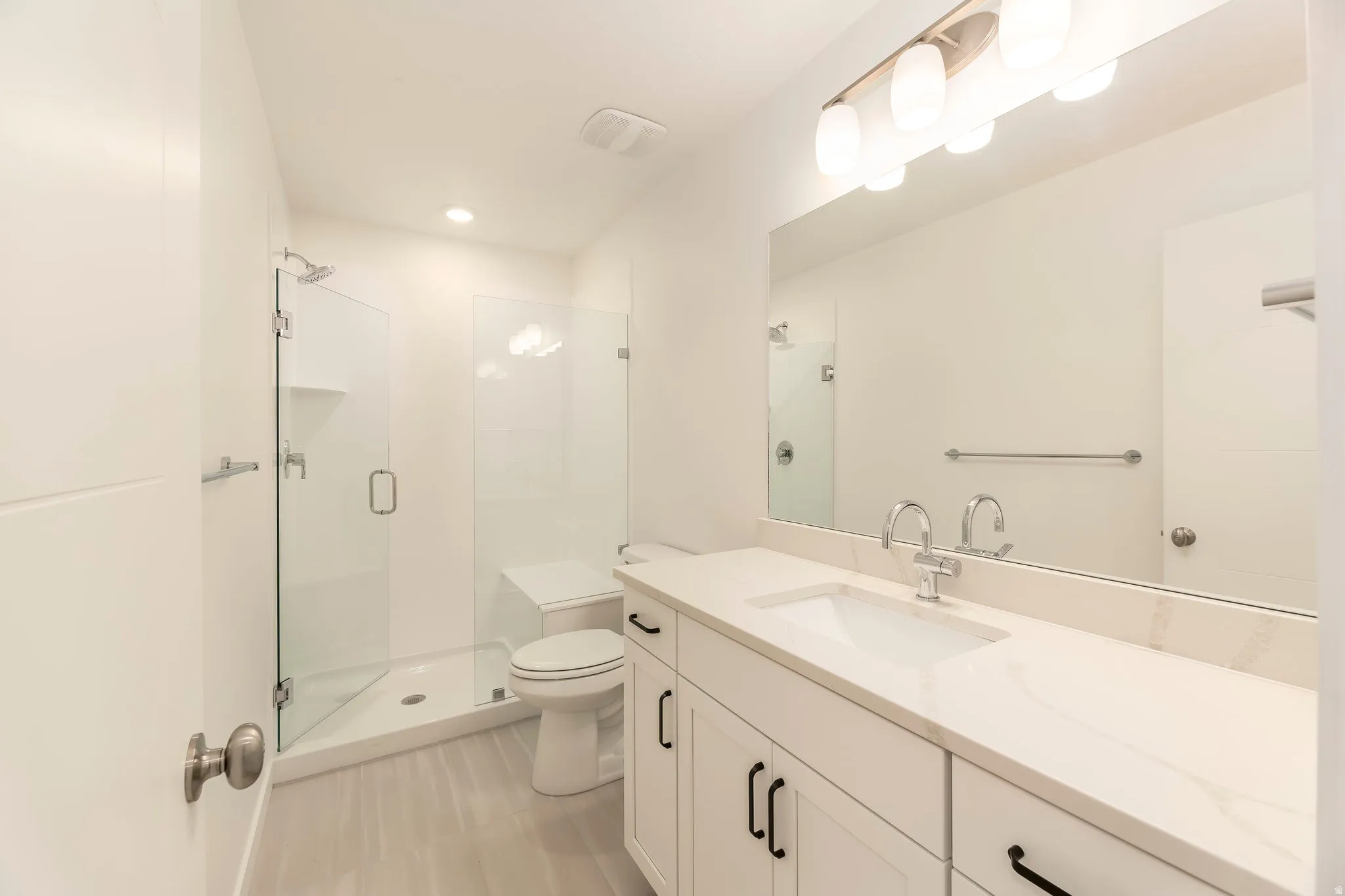 Bathroom featuring a frameless glass shower, a vanity with a white countertop, chrome fixtures, and a large wall-mounted mirror