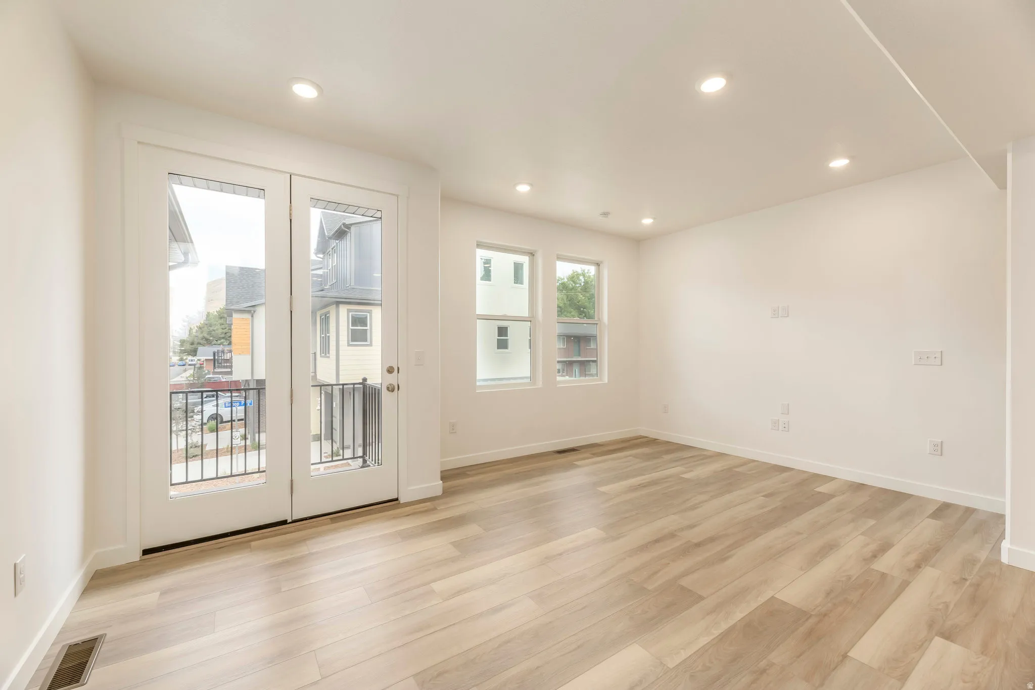 Recessed lighting, wood-finish flooring, white walls, multiple windows, and French doors to a balcony