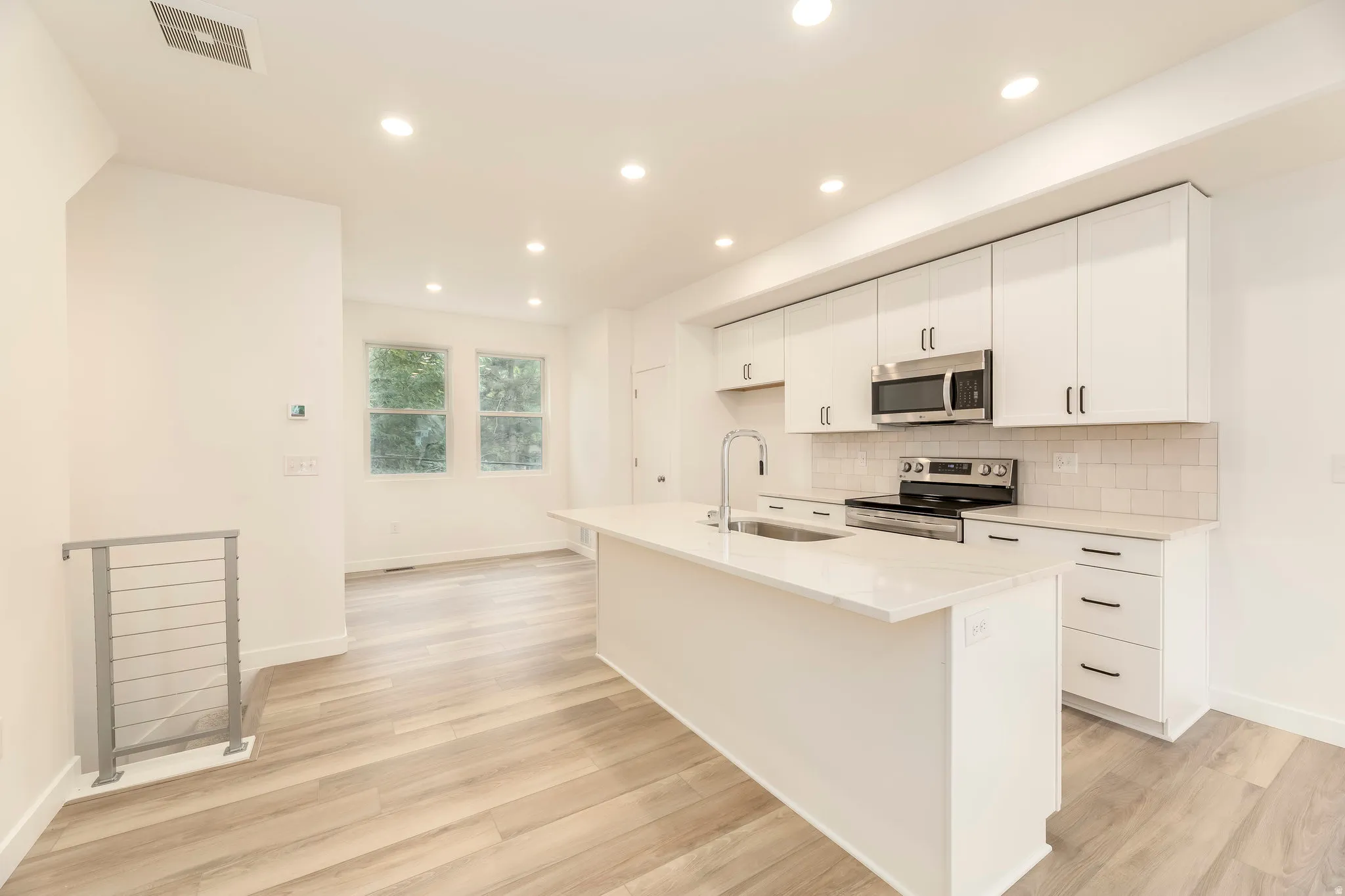 Modern kitchen featuring white cabinetry, stainless steel appliances, a center island with sink, and light wood-finish flooring