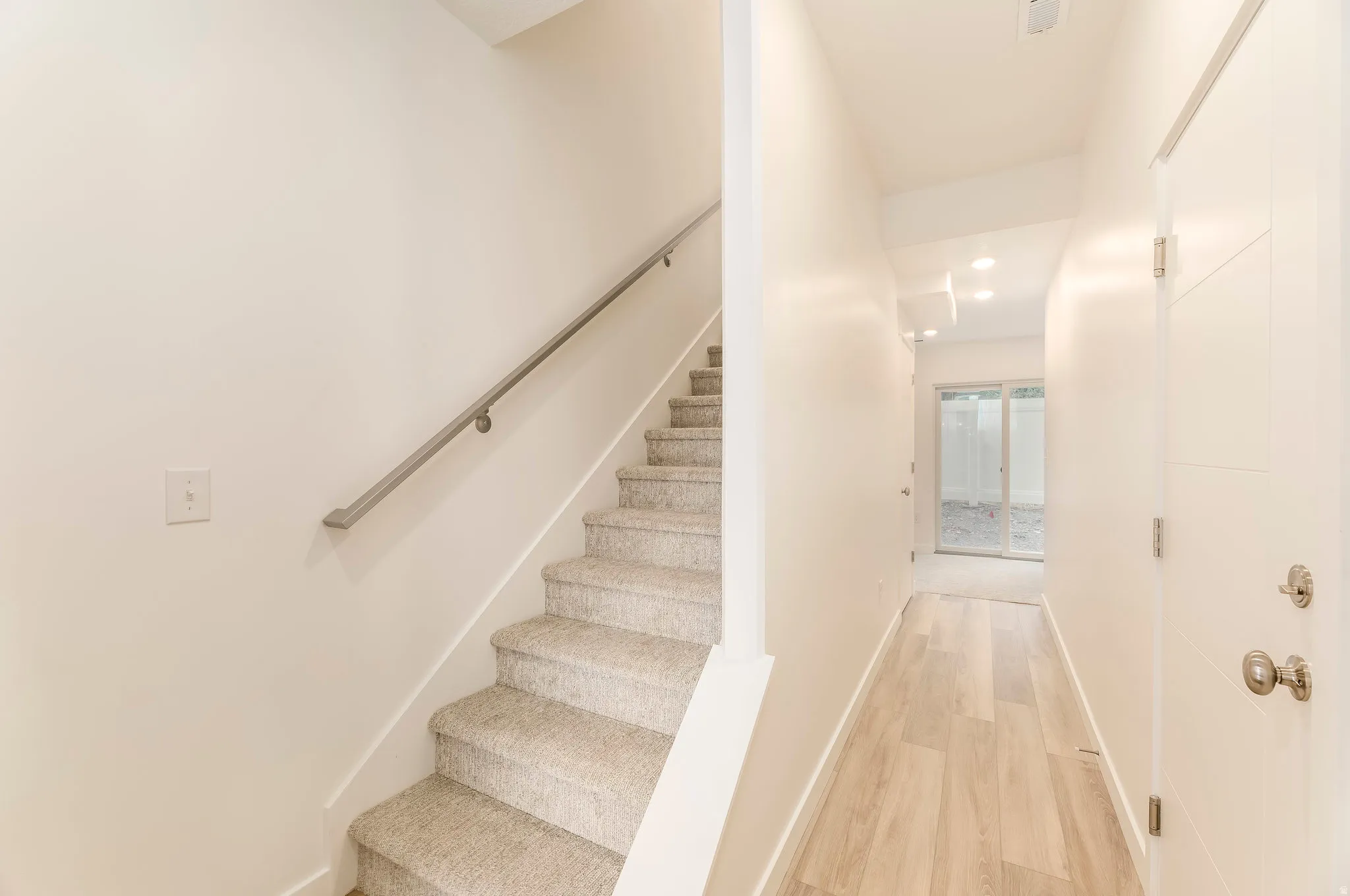 Light-toned wood-finish flooring, recessed lighting, and a modern white door with horizontal paneling
