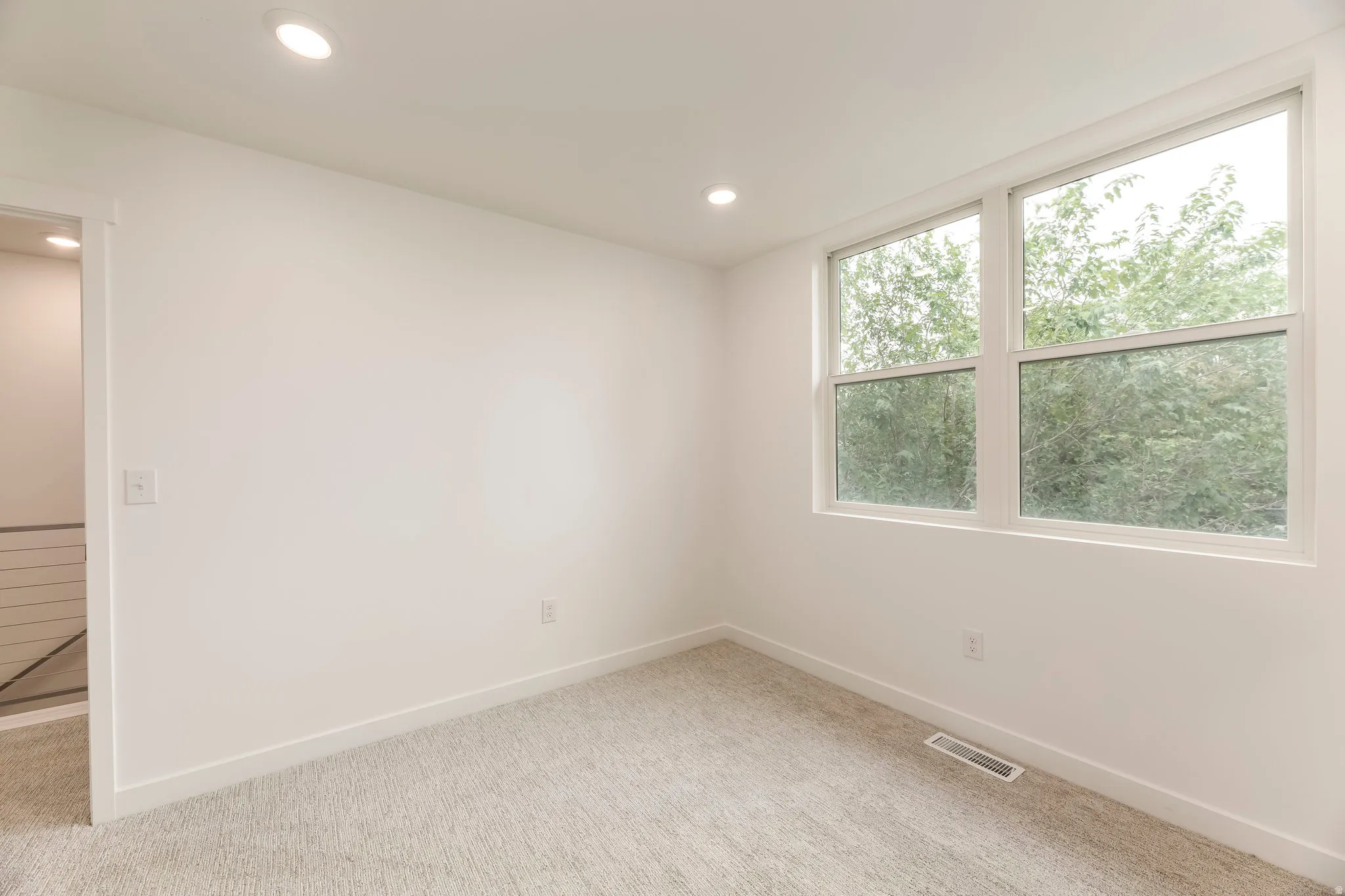 Recessed lighting, wall-to-wall carpeting, white walls, and a large window