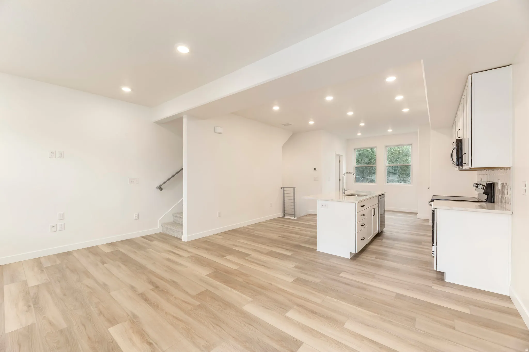 Wood-finish flooring throughout, recessed lighting, white kitchen cabinetry, stainless steel appliances, and a central kitchen island with an integrated sink