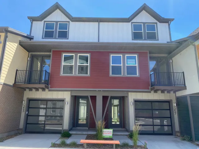 Contemporary facade featuring a gabled roofline, two upper-level balconies with black railings, two full-light garage doors, and a combination of red and white siding