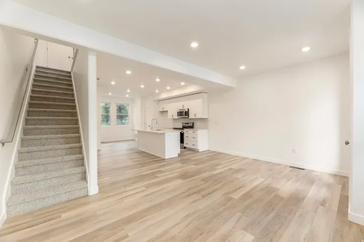 Recessed lighting, wood-finish flooring, white cabinetry, stainless steel appliances, and a central island with sink