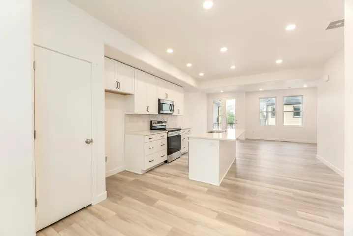 Kitchen featuring a central island with sink, white shaker-style cabinetry, and stainless steel appliances
