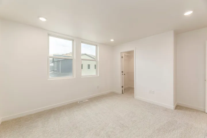 Recessed lighting illuminates this carpeted room featuring two windows and a closet with a bi-fold door