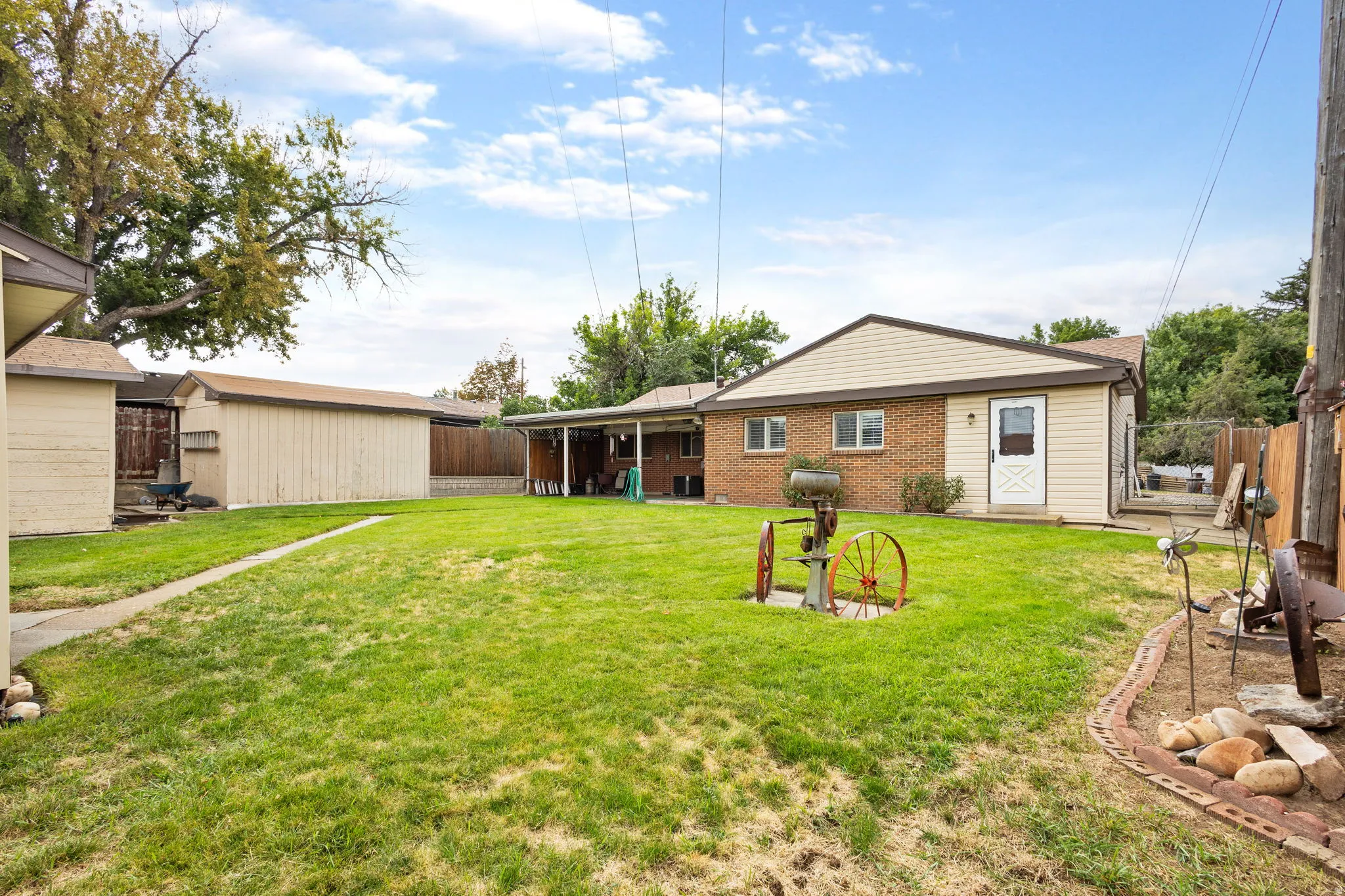 Expansive grassy area with a brick and siding exterior, covered patio, and two storage sheds