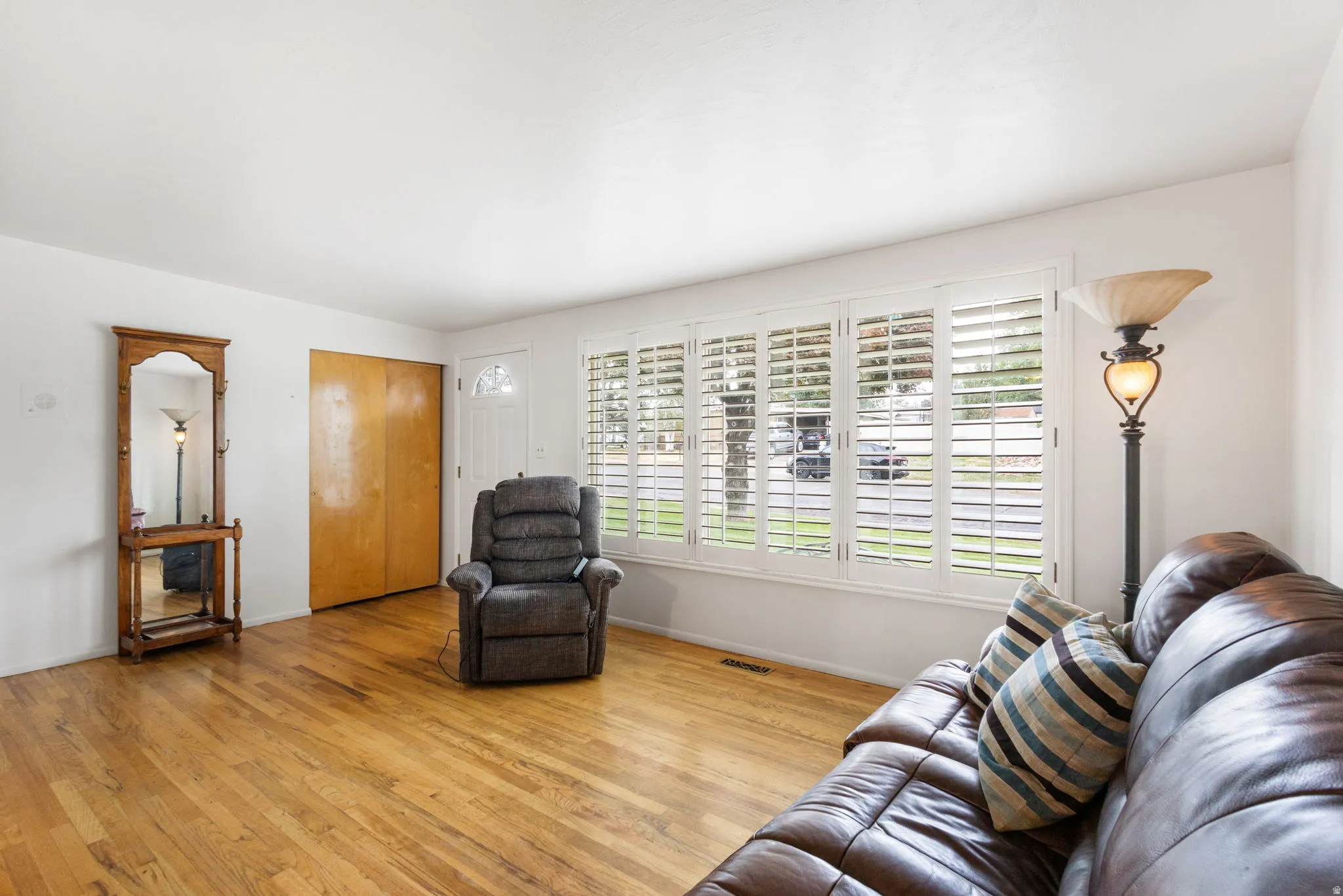 Hardwood flooring throughout, multiple windows with plantation shutters, white paneled entry door with frosted glass, and wood-finish closet doors