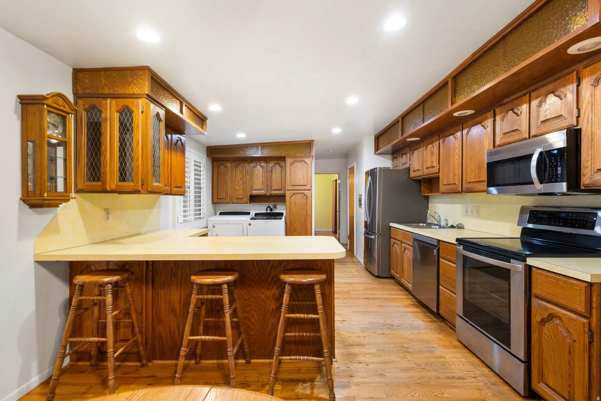 Kitchen featuring wood-finish flooring, recessed lighting, wood cabinetry, stainless steel appliances, and a built-in counter bar