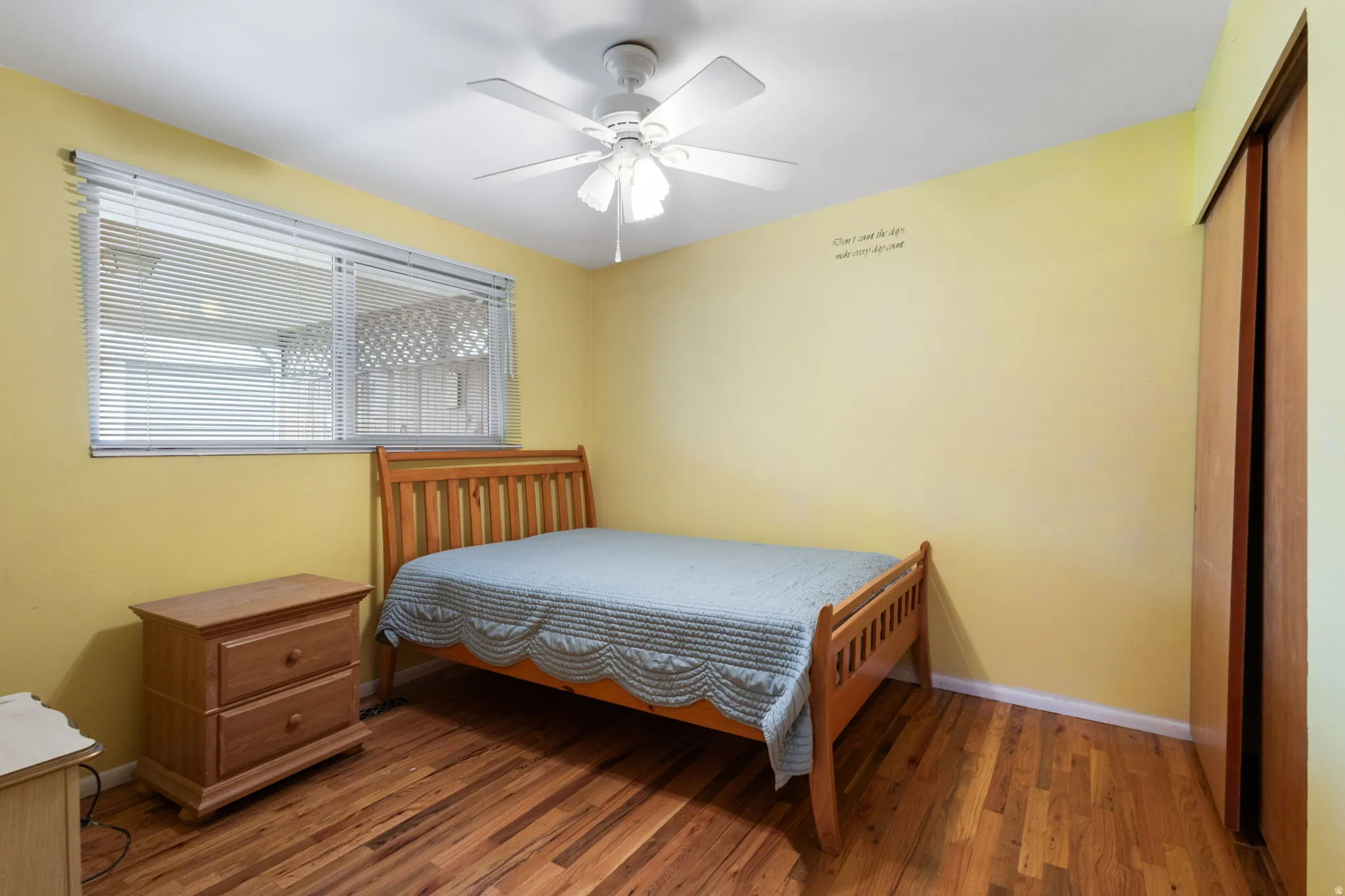 Wood-finish flooring, ceiling fan, window with horizontal blinds, and a built-in closet with wood doors