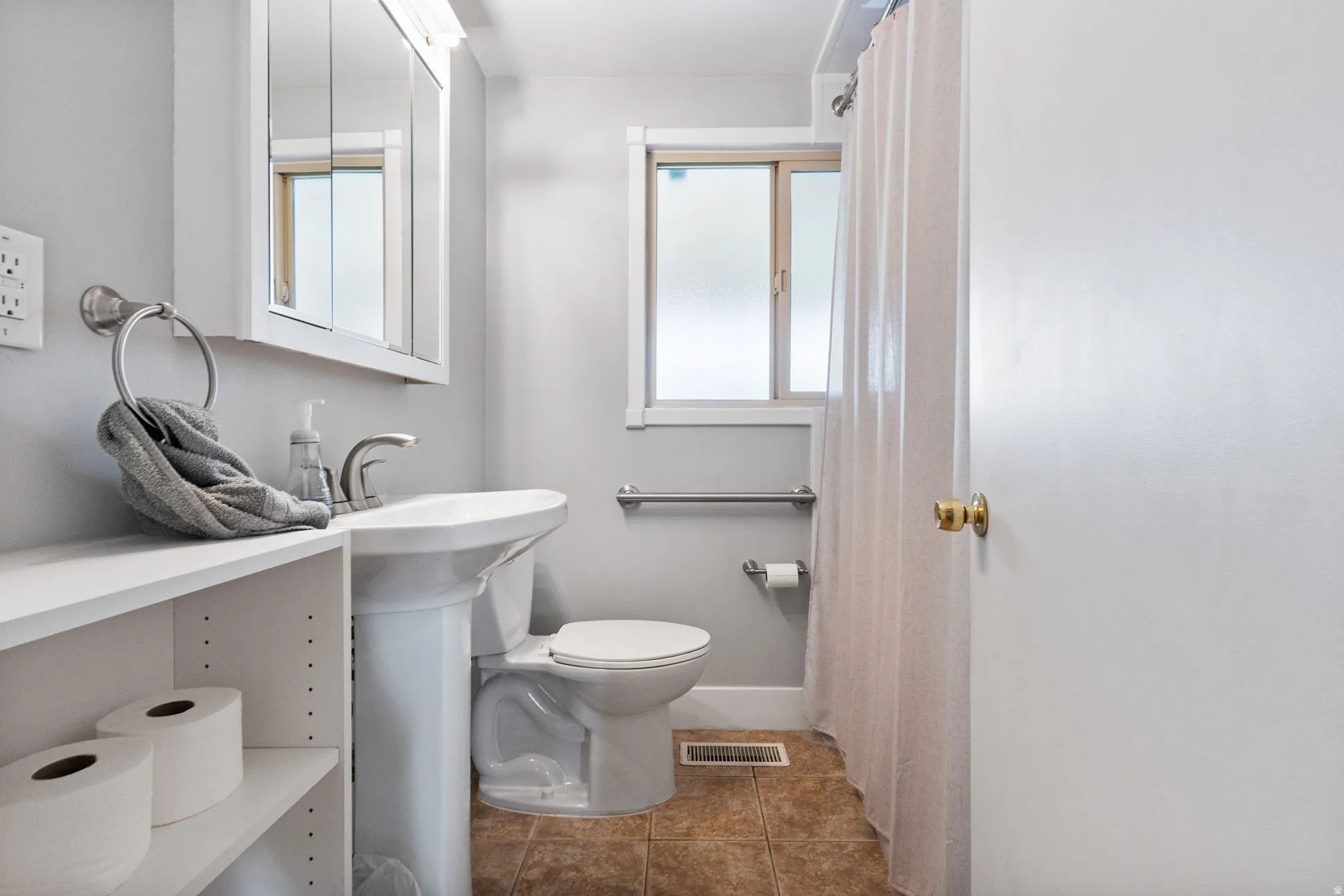 Bathroom featuring a pedestal sink, wall-mounted medicine cabinet, frosted window, and tiled flooring