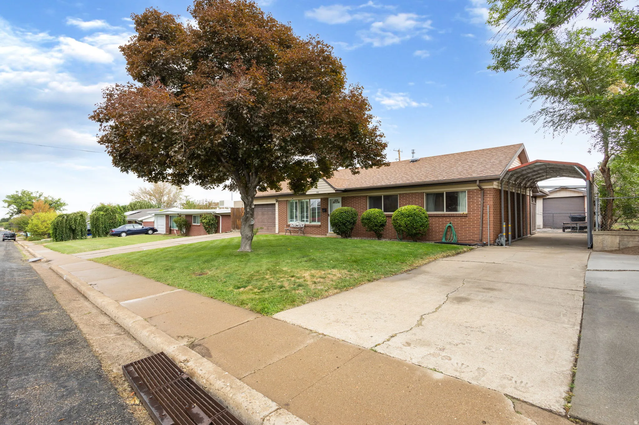 Brick exterior with a peaked roofline, front yard landscaping, a driveway, and an attached carport