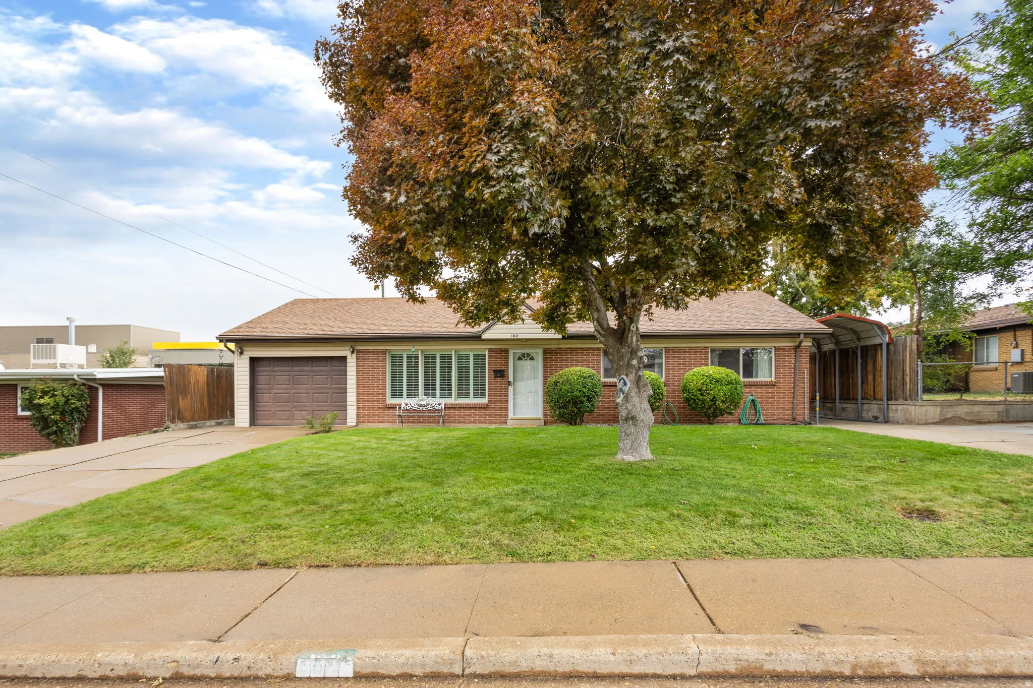 Brick exterior with a brown shingle roof, attached garage, concrete driveway, and a manicured front lawn