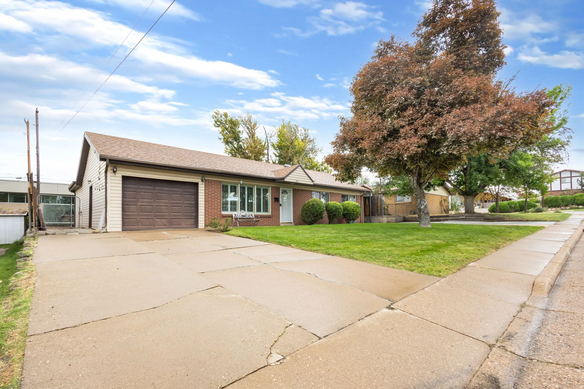 Brick and siding exterior with an attached garage, featuring a concrete driveway and sidewalk, and a mature tree