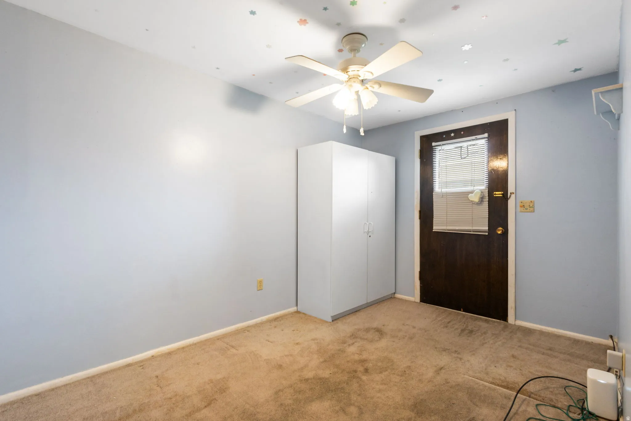 Wall-mounted ceiling fan with lighting, light blue wall paint, and brown carpet flooring