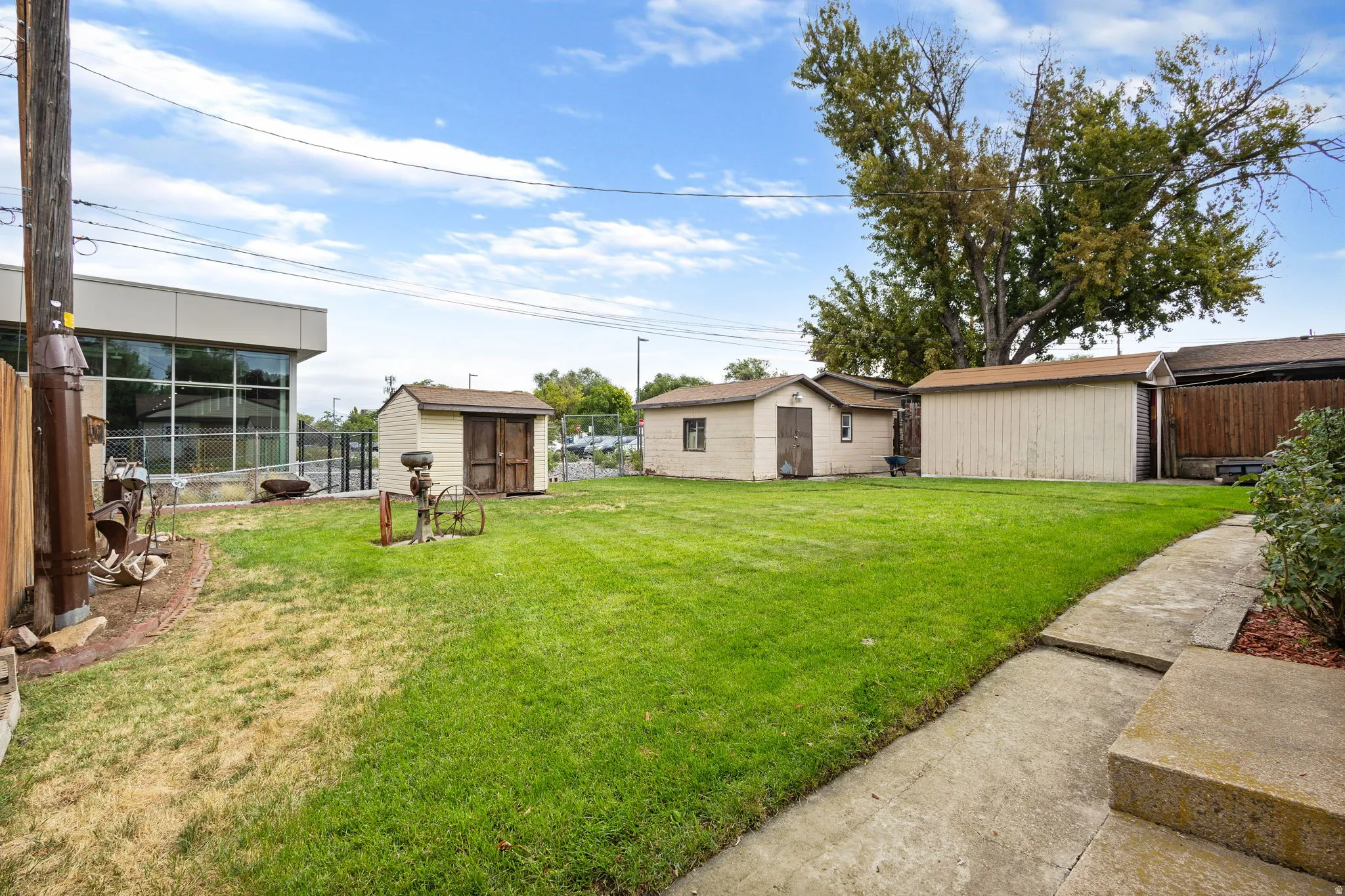 Expansive rear yard featuring a manicured lawn, concrete pathway, and three detached storage sheds
