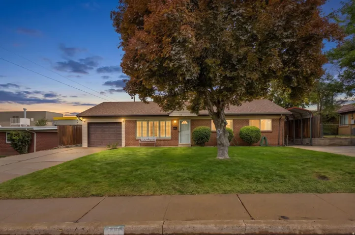 Brick exterior with an attached garage, paved driveway, and a front lawn with mature landscaping