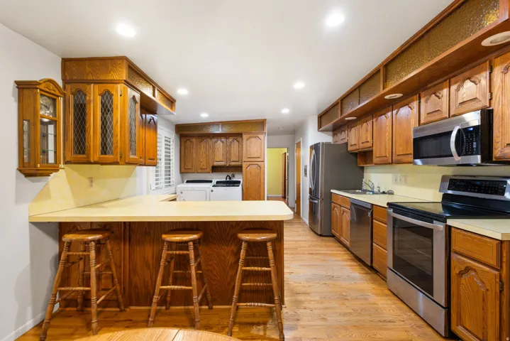 Kitchen featuring wood-finish flooring, recessed lighting, wood cabinetry, stainless steel appliances, and a built-in counter bar