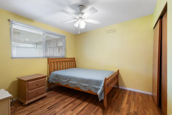 Wood-finish flooring, ceiling fan, window with horizontal blinds, and a built-in closet with wood doors