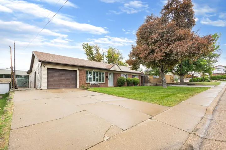 Brick and siding exterior with an attached garage, featuring a concrete driveway and sidewalk, and a mature tree