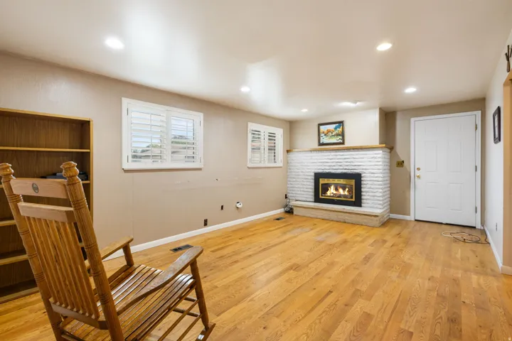 Hardwood flooring throughout, white brick fireplace with hearth, built-in shelving, recessed lighting, and windows with white plantation shutters