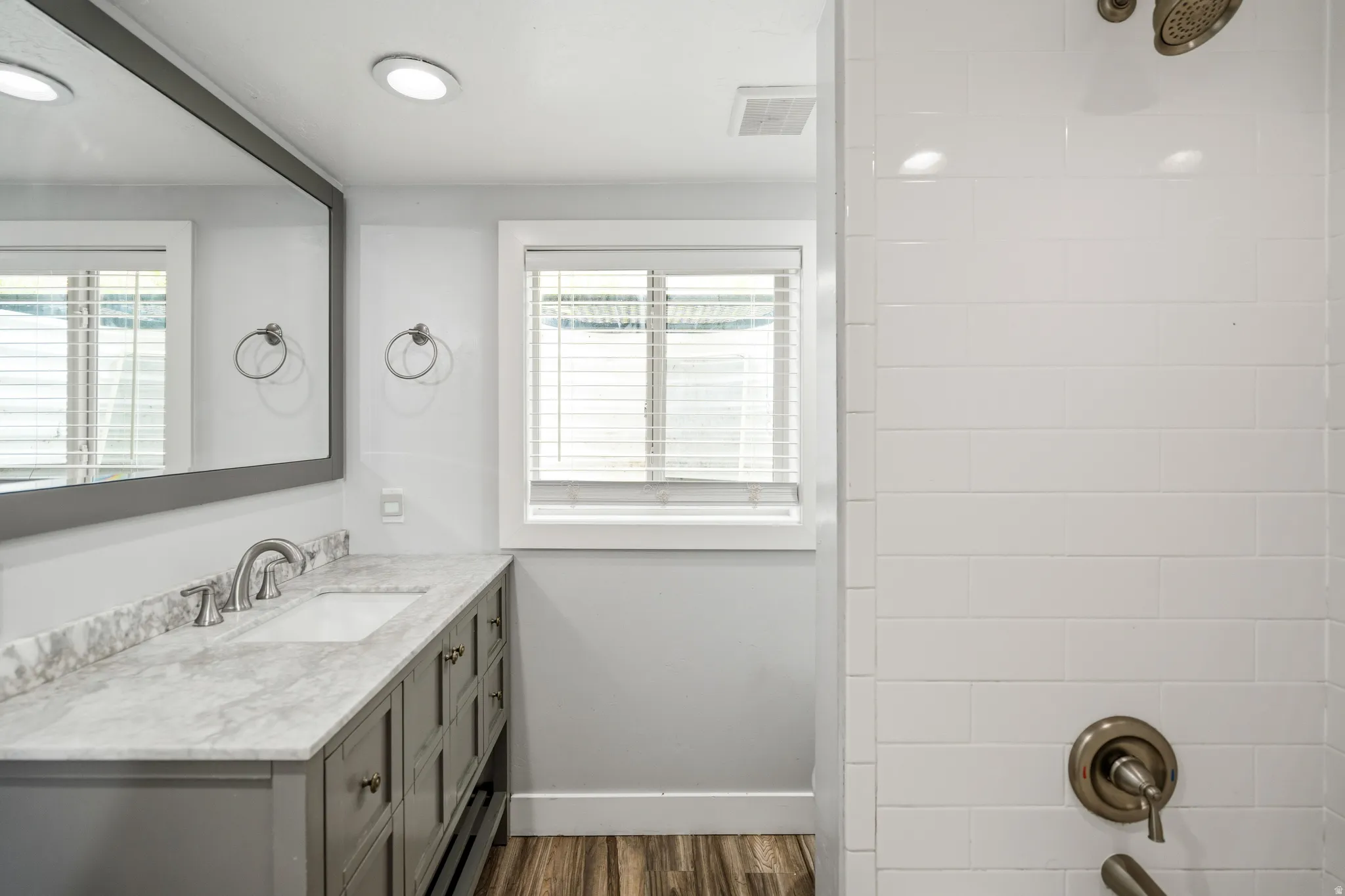 Bathroom featuring a gray vanity with a stone countertop, an undermount sink, and wood-finish flooring