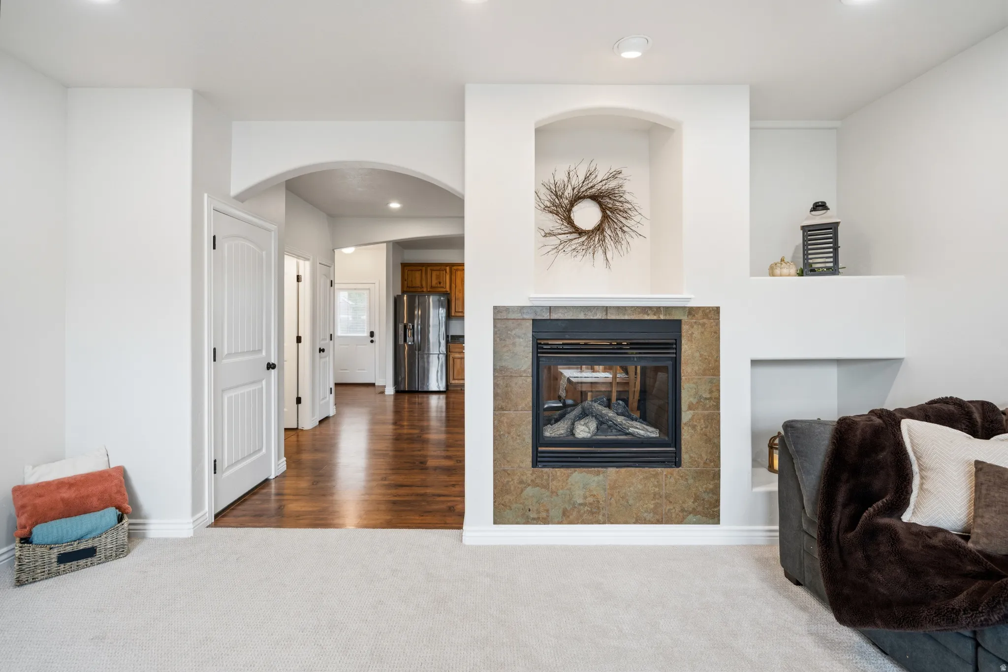 Recessed fireplace with stone-finish tile surround, built-in shelving, arched doorway, recessed lighting, and wood-finish flooring