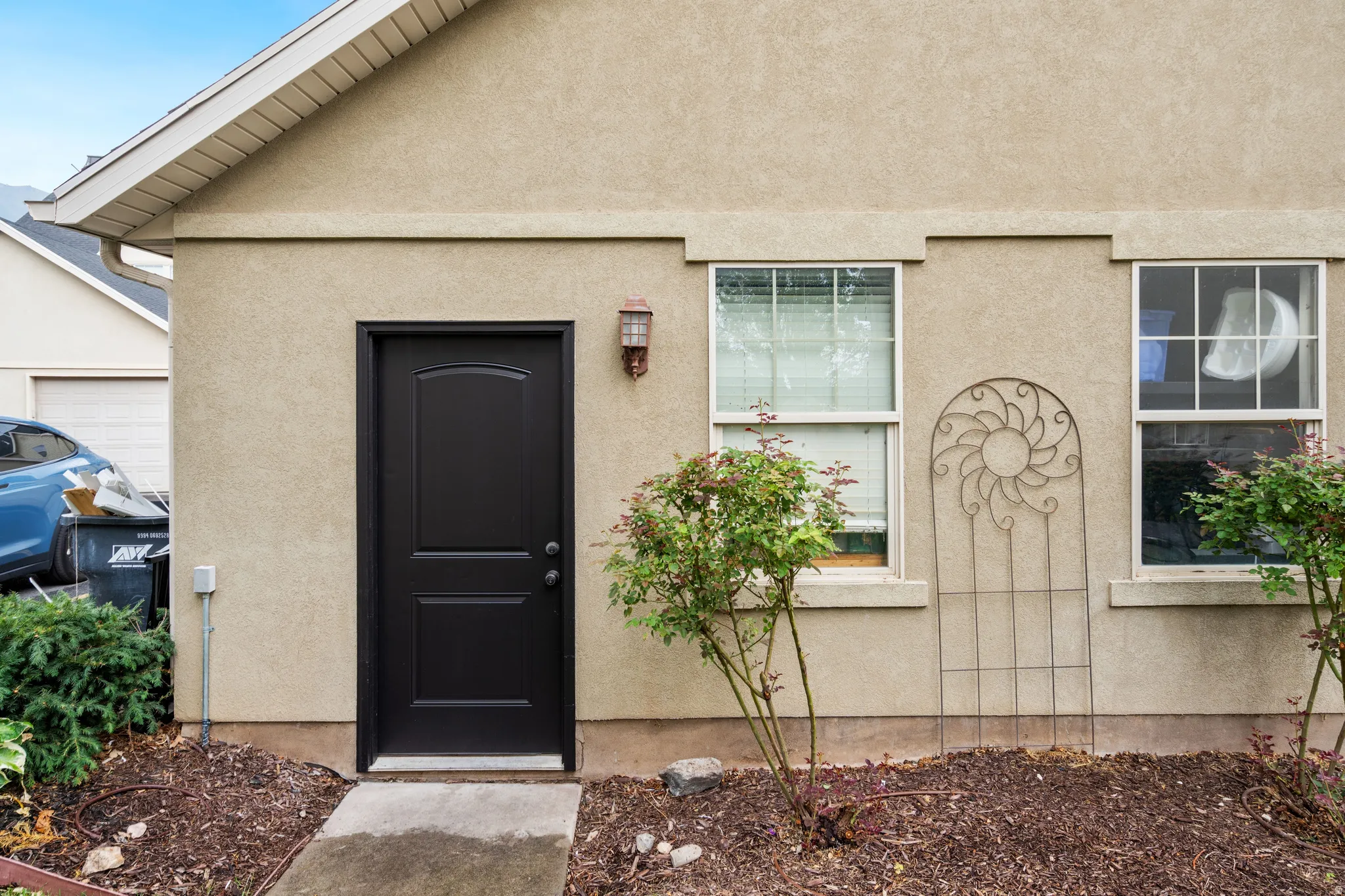 Stucco exterior with a dark-paneled entry door, two double-hung windows, and a decorative metal trellis