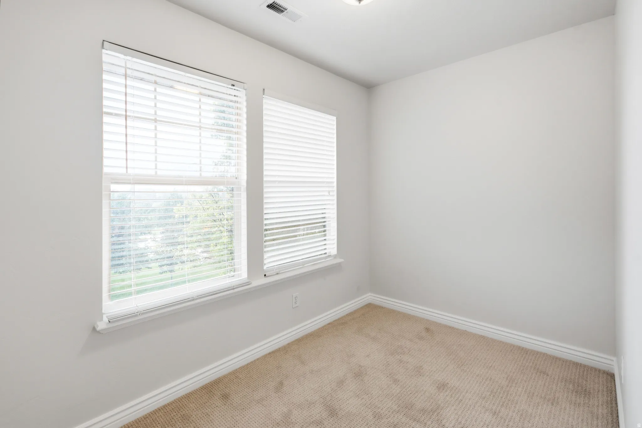 Recessed lighting, two windows with blinds, light-toned carpeting, and white wall finishes