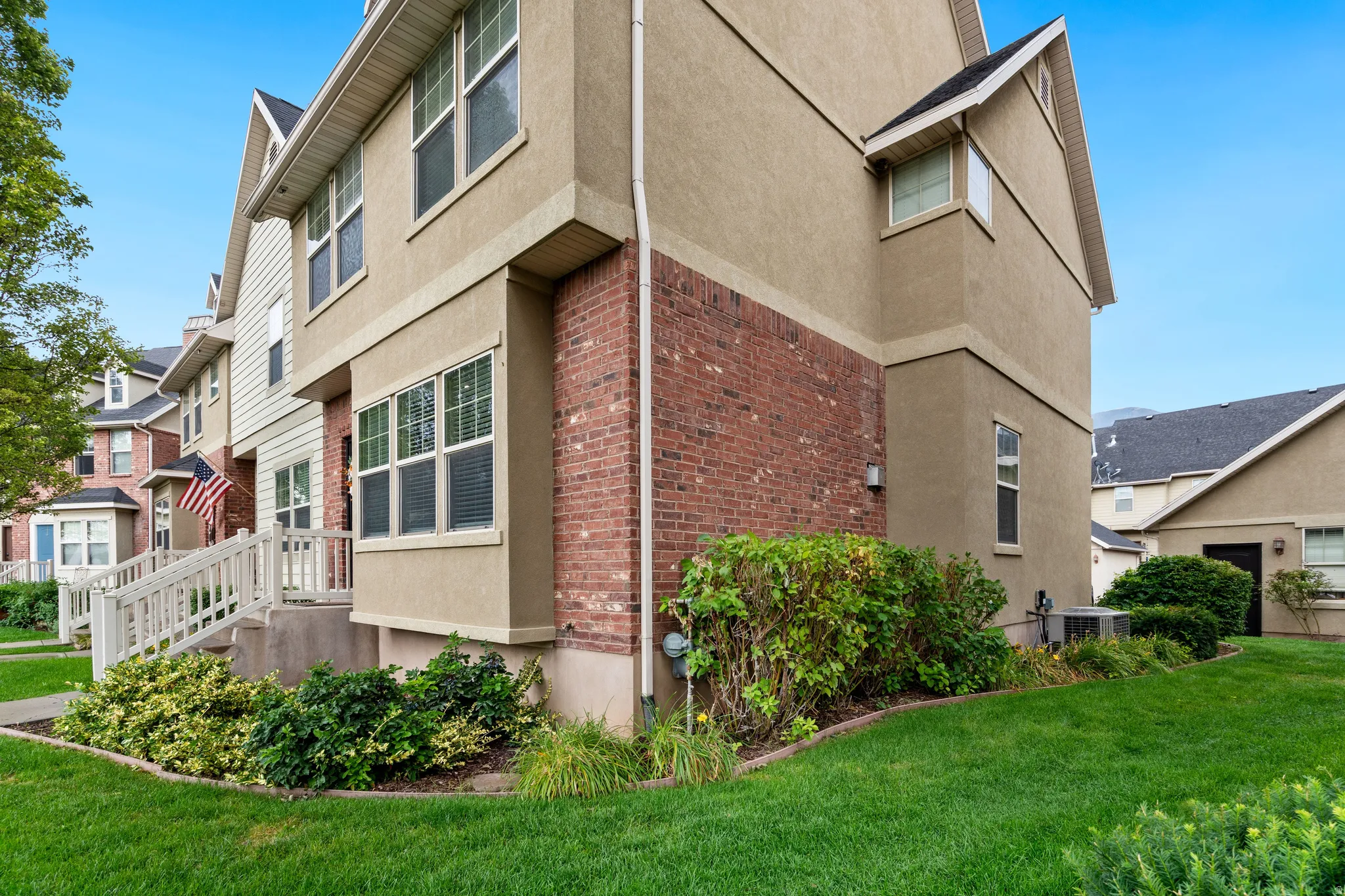 Stucco and brick exterior with multiple windows, pitched roofline, and established landscaping