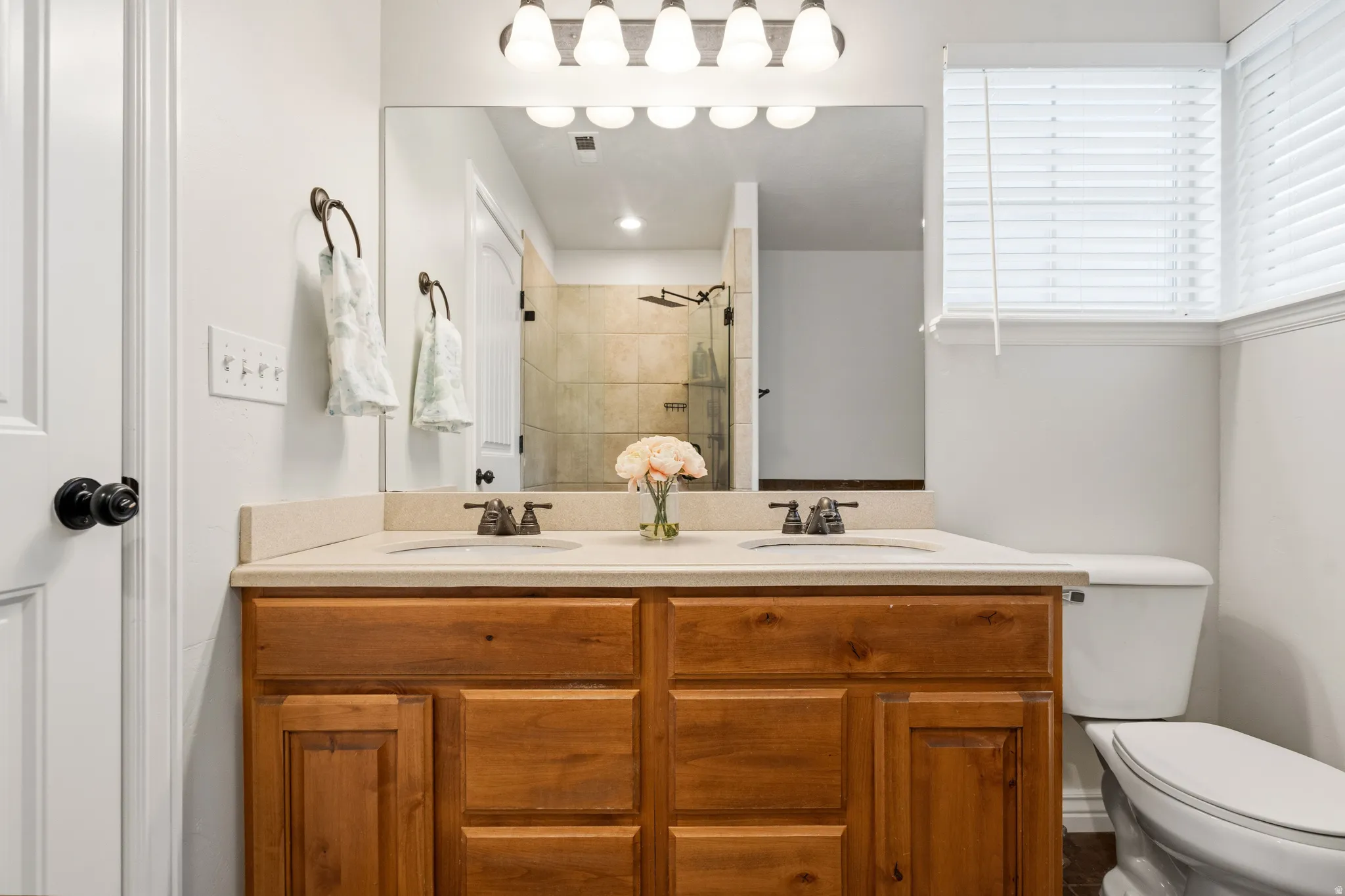 Dual sink vanity with wood-finish cabinetry, neutral countertop, and large wall-mounted mirror
