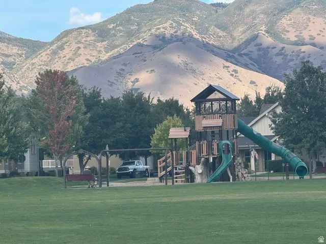 Expansive green space featuring a playground with slides and a swing set, all set against a backdrop of mountains