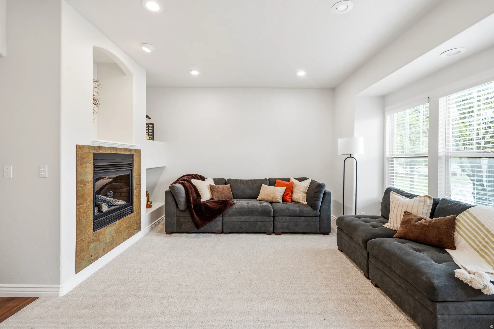 Recessed lighting, bay window, tile-surround fireplace, built-in shelving, and light-toned carpeting