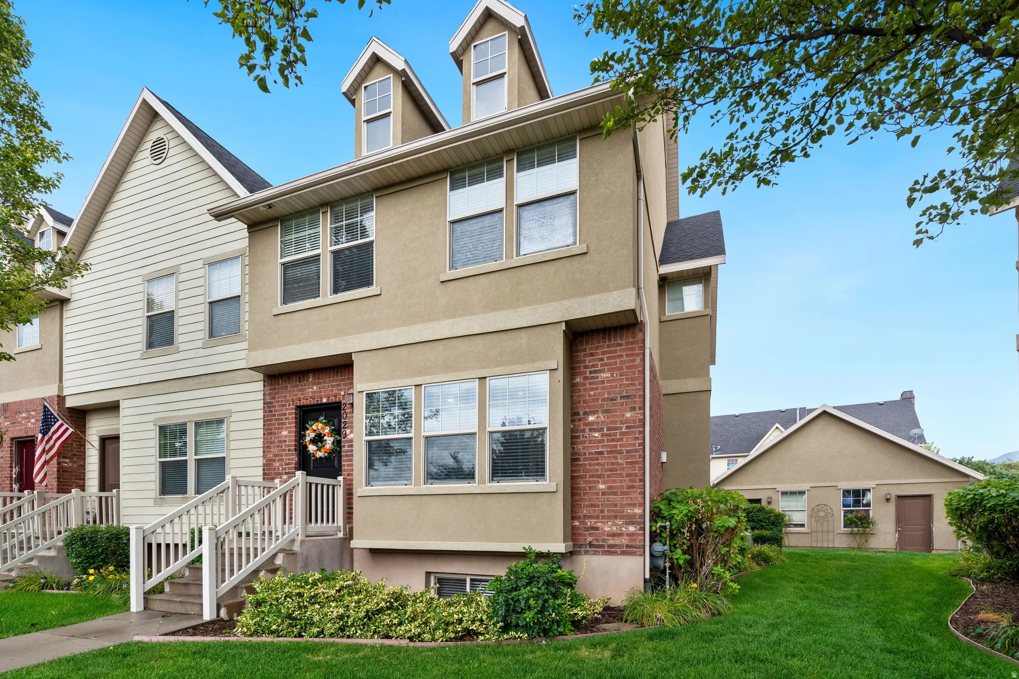 Stucco and brick exterior with dormer windows, covered entry, and landscaped grounds
