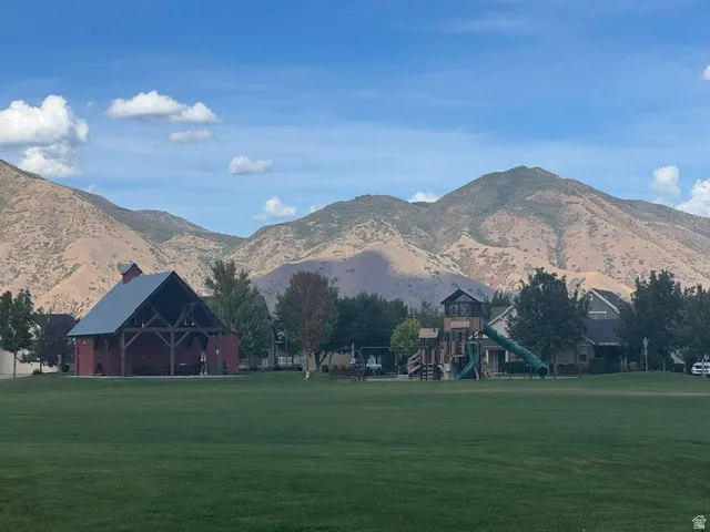Expansive green space featuring a red pavilion with an open-beam ceiling, a children's play structure with a slide, and a mountain backdrop