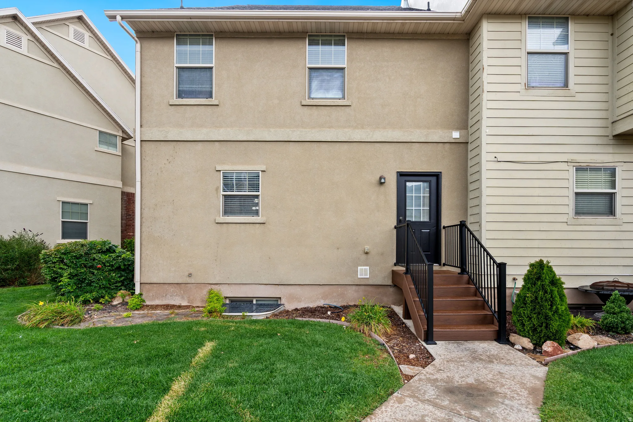 Rear exterior featuring a stucco finish, ground-level entry, composite stairs with black railings, and a concrete pathway
