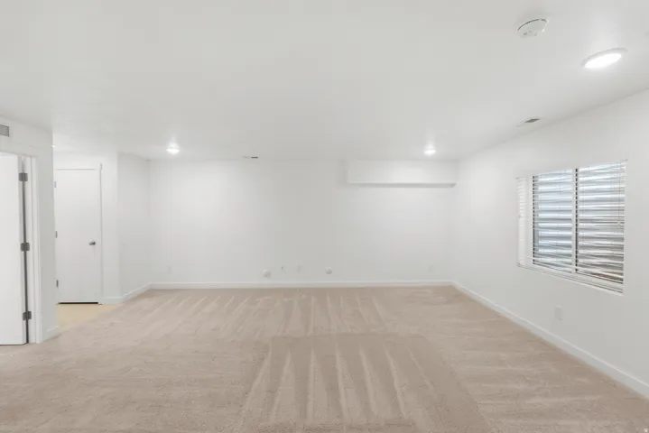 Recessed lighting illuminates neutral carpeting and white painted walls