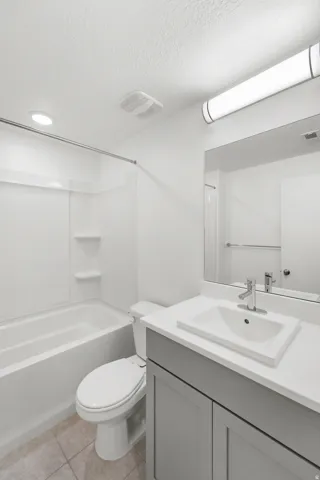 Bathroom featuring a white tub and shower combination, gray vanity with a single basin sink, and tile flooring