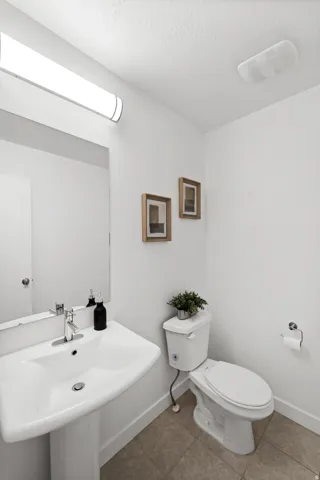 White pedestal sink with a chrome faucet, ceramic toilet, and tiled flooring