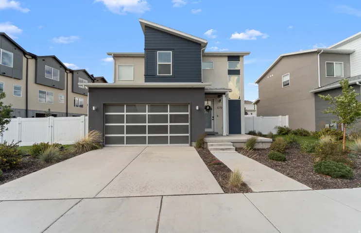 Contemporary architectural design featuring a multi-tone exterior, an attached two-car garage with a panel-window door, and a paved driveway