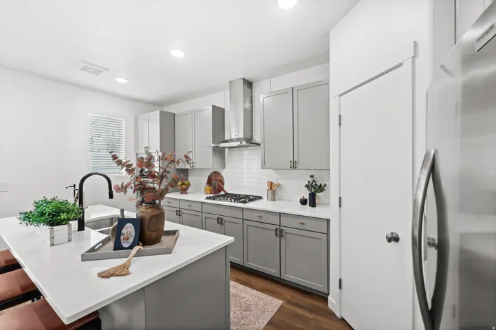 Modern kitchen featuring an island with an undermount sink, a matte black gooseneck faucet, light gray cabinetry, stainless steel appliances, and a subway tile backsplash