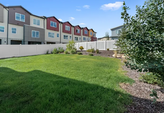 Expansive lawn featuring a white privacy fence, mulched landscape beds, and mature shrubs